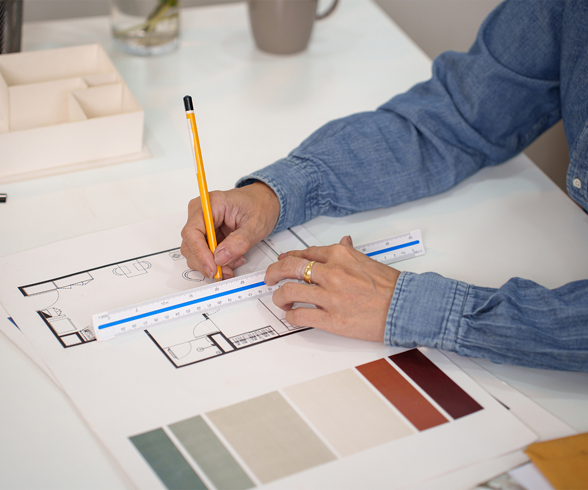 Hands measuring dining room floor plan for dining table layout and seating.
